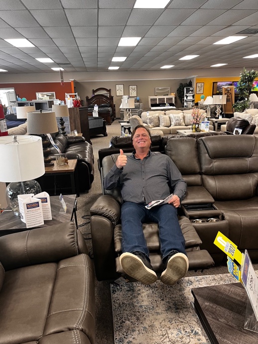 A PETERMAYER team member giving a thumbs up from a recliner on the showroom floor.