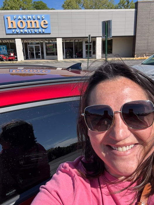 A PETERMAYER team member smiling in the parking lot of a Farmers Home Furniture store.